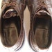 May include: A pair of brown leather shoes with laces. The shoes have a brogue design and are worn. The inside of the shoes is visible and shows the brown lining.