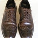 May include: Two brown leather oxford shoes with wingtip detailing and laces. The shoes have a dark brown color and a polished finish.
