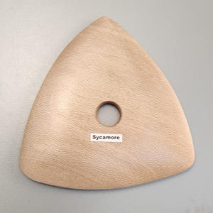 Puede incluir: Una herramienta de cerámica triangular de color marrón claro con un agujero central. La herramienta tiene una superficie texturizada y la palabra "Sycamore" está impresa en una pequeña etiqueta blanca.