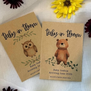 May include: Two brown paper envelopes with wildflower seed mix inside. The envelopes have a baby shower theme with the text "Baby in Bloom" and illustrations of an owl and a bear. The text on the envelopes also includes the baby's name and expected arrival date.