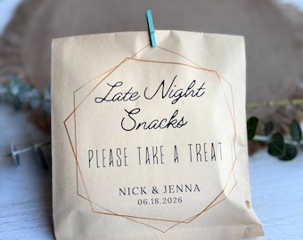 May include: A tan paper snack bag with the text "Late Night Snacks PLEASE TAKE A TREAT" in black script and block letters. The bag is decorated with a gold geometric design and held closed with a teal clothespin. The names "Nick & Jenna" and the date "06.18.2026" are printed below.