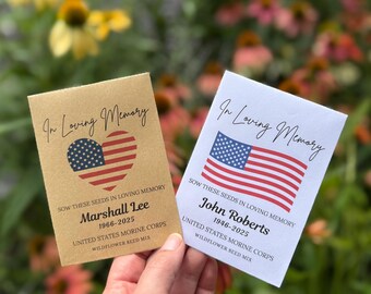 May include: Two seed packets with patriotic designs. One features a heart-shaped American flag, the other a full flag. Both packets read "In Loving Memory" and include names, dates, and "United States Marine Corps".