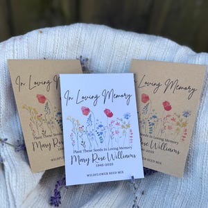 May include: Three seed packets with floral designs and the text "In Loving Memory." The packets are in shades of brown and white, with watercolor illustrations of wildflowers. The text includes names and dates.