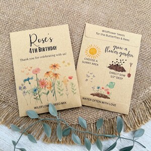 May include: Two seed packets on a burlap surface. One reads "Rose's 4th Birthday" with floral illustrations. The other says "Wildflower Seeds for the Butterflies & Bees" with planting instructions. The packets are tan with black and colorful text and illustrations.