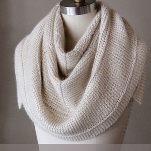 Puede incluir: Un chal de punto blanco con un patrón de punto sencillo y un borde festoneado. Patrón de tejido de punto.