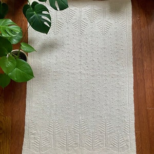 May include: A white knitted throw blanket with a geometric pattern. The blanket has a subtle texture and a simple design.