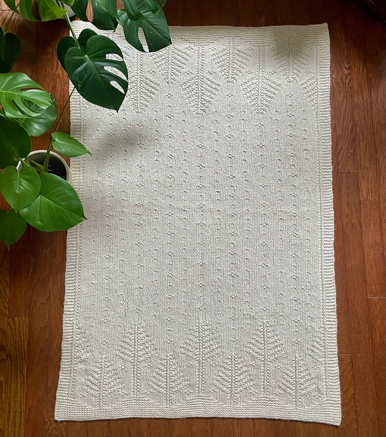 May include: A white knitted throw blanket with a geometric pattern. The blanket has a subtle texture and a simple design.