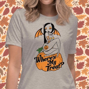 May include: A heather gray t-shirt featuring a Halloween-themed graphic. The design includes a bat-winged figure sitting on a pumpkin, with the text "Where's My Treat?" in a stylized font. The artwork has orange and black accents.