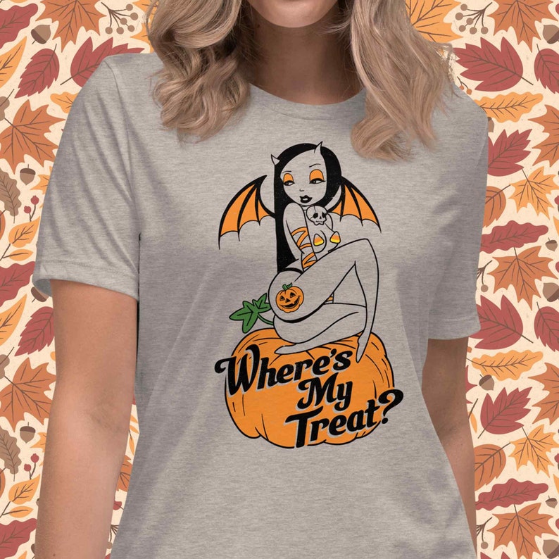 May include: A heather gray t-shirt featuring a Halloween-themed graphic. The design includes a bat-winged figure sitting on a pumpkin, with the text "Where's My Treat?" in a stylized font. The artwork has orange and black accents.