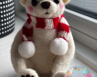 May include: A handmade white felt bear with a red and white striped scarf and pom-poms. The bear has black eyes, a brown nose, and pink cheeks. The bear's paws are black. The bear is sitting on a white surface.