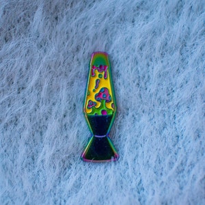 Może przedstawiać: Szpilka z emalii w tęczowych kolorach, w kształcie lampy lawowej z żółtym i różowym grzybem w środku.