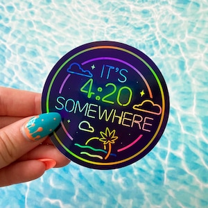 May include: A black iridescent sticker with a rainbow outline. The sticker says "It's 4:20 Somewhere" with a palm tree and waves in the background.