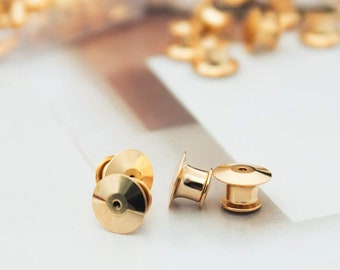 以下が含まれることがあります： 衣服にバッジやその他のアイテムを取り付けるための、金色の金属製のピンバックが4つ。ピンバックは、丸くて平らなベースと、小さな隆起した中心を持っています。