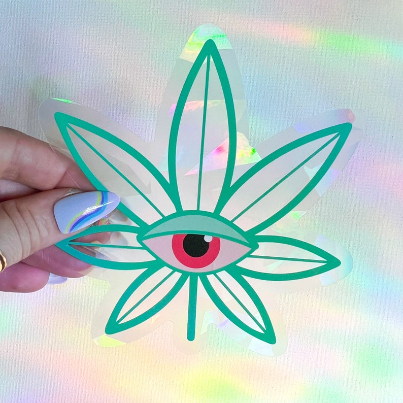 K&ouml;nnte beinhalten: Ein holografischer Aufkleber mit einem gr&uuml;nen Marihuanablatt und einem roten Auge in der Mitte.