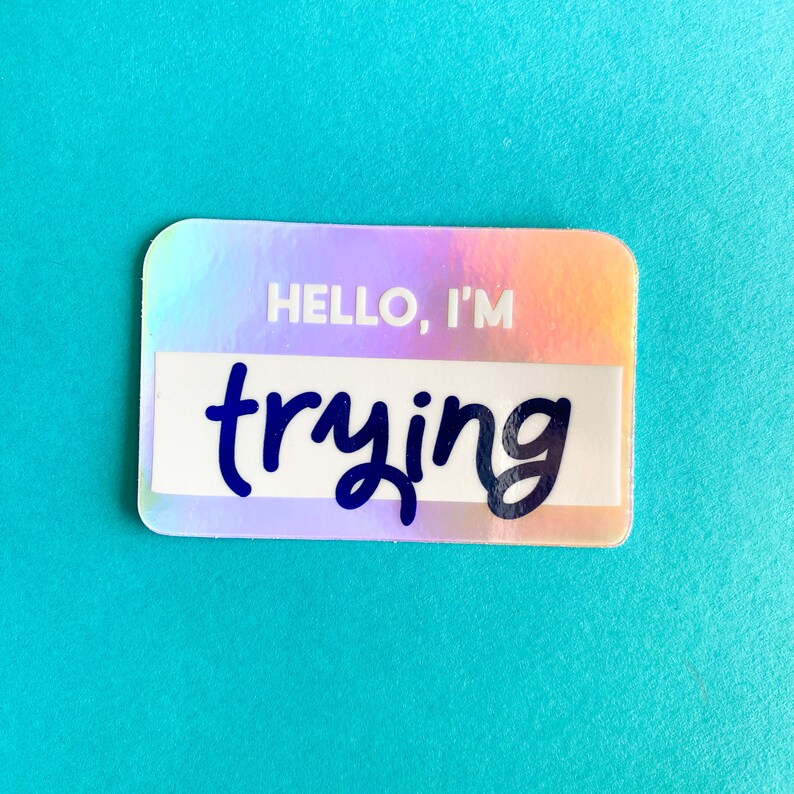 以下が含まれることがあります： 黒い文字で「HELLO, I'M trying」と書かれたホログラフィックステッカーです。