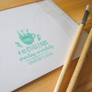 Puede incluir: Un sello verde con una imagen estilizada de una taza de caf&eacute; con pinceles dentro. El texto "ChelZart creating colorfully chelzart.com" est&aacute; debajo de la imagen.