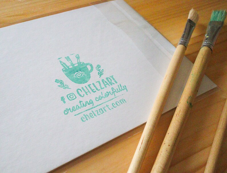 Puede incluir: Un sello verde con una imagen estilizada de una taza de caf&eacute; con pinceles dentro. El texto "ChelZart creating colorfully chelzart.com" est&aacute; debajo de la imagen.