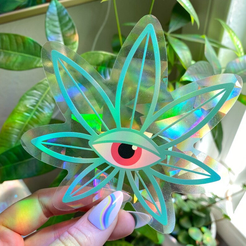 K&ouml;nnte beinhalten: Ein holografischer Aufkleber mit einem gr&uuml;nen Marihuanablatt und einem roten Auge in der Mitte.