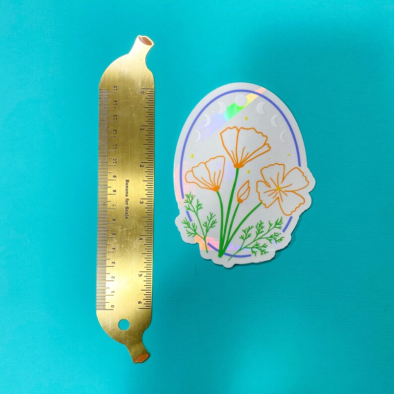 May include: A white sticker with a holographic finish featuring a line drawing of three orange California poppies with green leaves and stems. The sticker is oval shaped and has a blue outline. The background is a light blue colour.