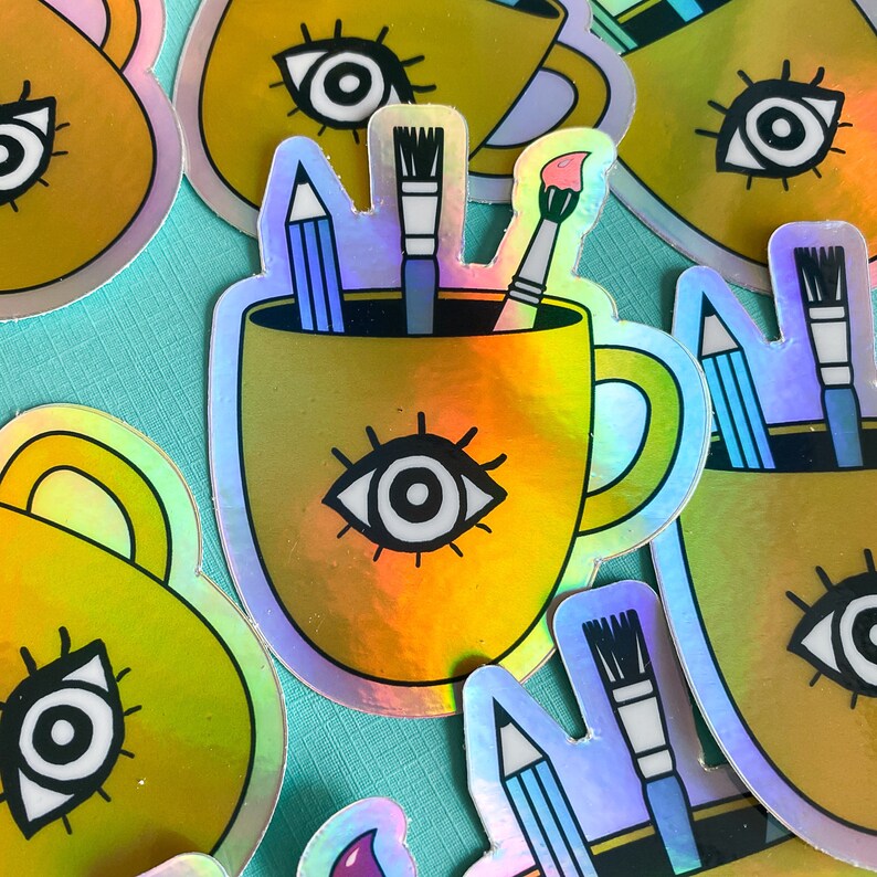 Puede incluir: Un conjunto de pegatinas hologr&aacute;ficas de colores con una taza con un dise&ntilde;o de ojo, l&aacute;pices y pinceles. Las pegatinas son perfectas para agregar un toque de fantas&iacute;a a las computadoras port&aacute;tiles, las botellas de agua o los diarios.
