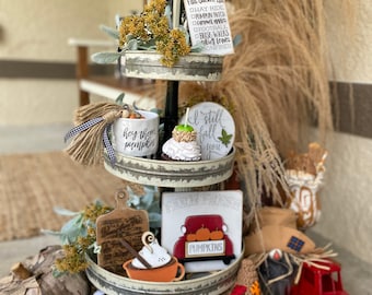 Könnte beinhalten: Ein dreistöckiger Tablett, dekoriert mit Herbst-Motiven, darunter ein Holzschild mit der Aufschrift "Fall Bucket List", ein Holzschild mit der Aufschrift "I still fall for you", ein Holzschild mit der Aufschrift "Farm Fresh Pumpkins", ein Holzschild mit der Aufschrift "Hey there pumpkin", ein Holzschild mit einem roten LKW und Kürbissen, ein Holzschild mit drei Kürbissen, eine Tasse mit Schlagsahne, ein kleiner roter LKW, eine Vogelscheuche und ein schwarz-weiß karierter Kürbis.