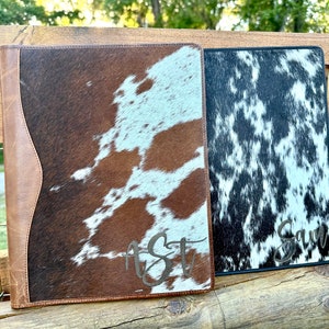 Puede incluir: Dos carpetas de cuero de vaca marrón y negro con monogramas personalizados. La carpeta de la izquierda tiene el monograma "AST" y la carpeta de la derecha tiene el monograma "Sam".