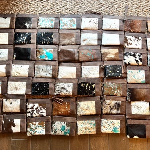 May include: A display of leather clutch bags with cowhide panels. The bags showcase diverse patterns and colours, such as black and white, brown, and turquoise. Each bag has a brown leather frame and a zip closure.