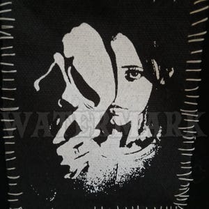 May include: Black and white graphic of a woman's face with a mask. The image is stitched onto a black fabric. The word "WATERMARK" is partially visible in the lower left corner.