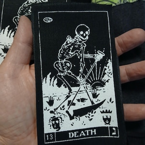 May include: Black rectangular patch featuring a white illustration of a skeleton with a scythe, labeled "DEATH" with the number "13". The patch has a white border and is likely for clothing or accessories.