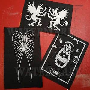 May include: Three black fabric patches with white illustrations. One patch features two winged creatures, another a skeletal design, and the third depicts a deity with multiple arms and a necklace.