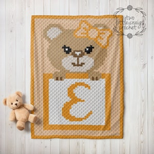 May include: A crochet baby blanket with a brown bear holding a block with the letter E on it. The bear is wearing a yellow bow. The blanket is made with a variety of colors, including brown, yellow, and white.