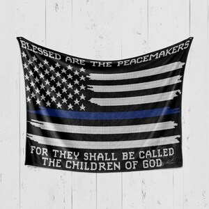 May include: Black and white American flag with a blue stripe across the middle. The flag has the words "Blessed are the peacemakers" at the top and "For they shall be called the children of God" at the bottom.