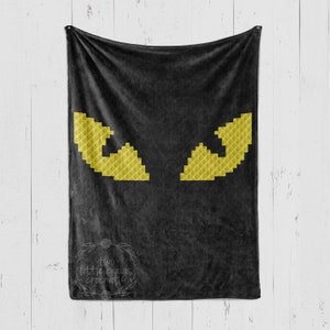 May include: Black fleece blanket with two large yellow eyes embroidered on it. The blanket has the text "two little craigs crochet" in a circle at the bottom right corner.