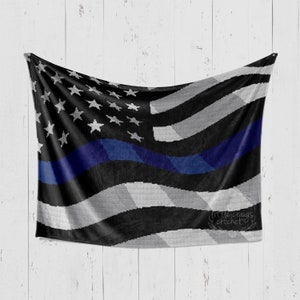 May include: A crocheted American flag blanket with a blue line running horizontally across the middle. The blanket is draped over a white wooden surface. The text "littlecraigs crochet" is in the lower right corner.
