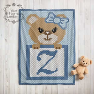 May include: A crochet baby blanket with a blue background and a brown bear holding a blue letter Z. The bear is wearing a blue bow.