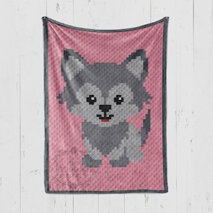 May include: A pink and gray crocheted blanket featuring a pixelated image of a gray wolf. The wolf has black eyes and a red tongue. The blanket has a dark gray border and the text "two little things crochet" in the bottom left corner.