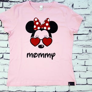 May include: Pink t-shirt with a black and white Mickey Mouse design wearing red heart-shaped sunglasses and a red and white polka dot bow. The text "mommy" is printed below the design.