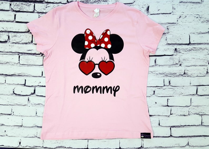 May include: Pink t-shirt with a black and white Mickey Mouse design wearing red heart-shaped sunglasses and a red and white polka dot bow. The text "mommy" is printed below the design.