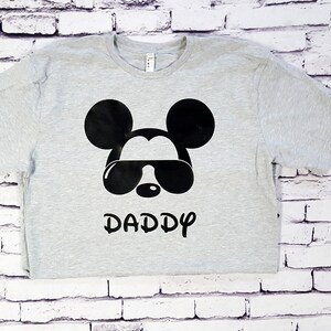 May include: A gray t-shirt with a black Mickey Mouse design wearing sunglasses and the word "DADDY" underneath.