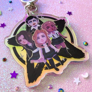 May include: A clear acrylic keychain featuring a group of four stylized female figures. The figures are depicted in a cartoon style, with a black and green background. The keychain has a silver clasp and is surrounded by decorative stars.