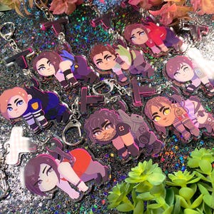 May include: A set of eight colorful character charms with different designs. The charms are made of clear acrylic with glitter embedded in the background. Each charm features a different character with a unique expression and pose. The charms are attached to silver keychains.