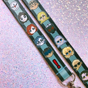 May include: A black and blue lanyard with a repeating pattern of cartoon faces. The lanyard has a silver metal clip.