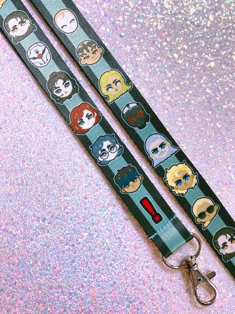 May include: A black and blue lanyard with a repeating pattern of cartoon faces. The lanyard has a silver metal clip.