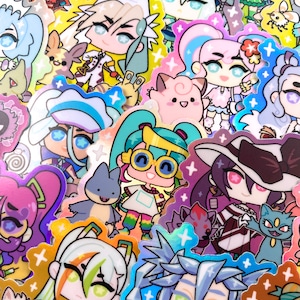 May include: A collection of colourful holographic stickers featuring anime-style characters with large eyes and bright colours. The stickers have a shiny, iridescent finish and feature various characters, including a pink and blue character with a flower crown, a green character with glasses, and a purple character with a witch's hat.