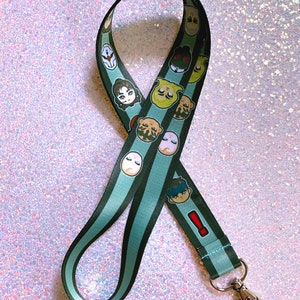 May include: A green and black striped lanyard with cartoon character faces printed on it. The lanyard has a silver metal clip.