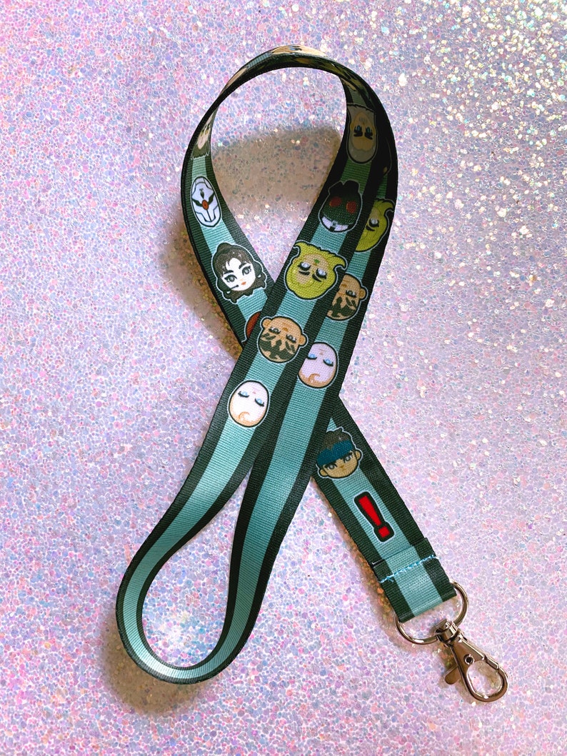 May include: A green and black striped lanyard with cartoon character faces printed on it. The lanyard has a silver metal clip.