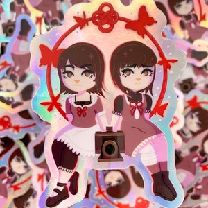 May include: Two cartoon girls with brown hair and red bows are sitting side-by-side. They are wearing white dresses with red bows and black shoes. They are holding a vintage camera in front of them. The background is a pink and white swirl with red butterflies and a red knot.