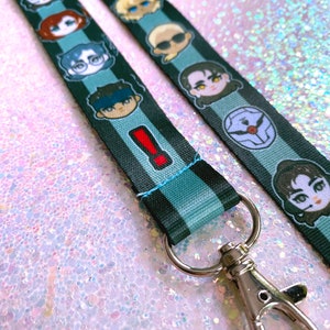 May include: A black and blue lanyard with a variety of cartoon characters printed on it. The lanyard has a silver metal clip.