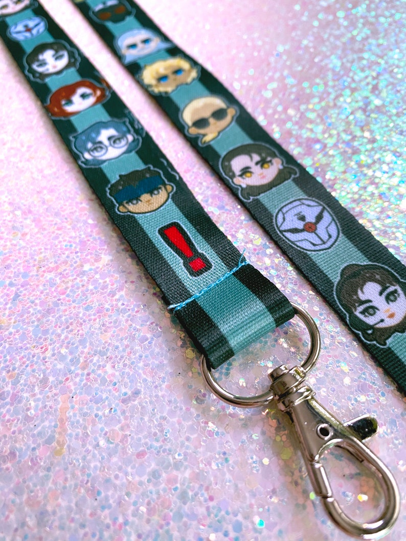 May include: A black and blue lanyard with a variety of cartoon characters printed on it. The lanyard has a silver metal clip.
