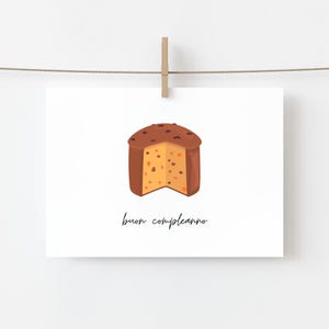 May include: A white card with a drawing of a panettone cake, cut to show the inside. The cake is brown with dark brown spots on top and a yellow interior. The words "buon compleanno" are written below the cake.